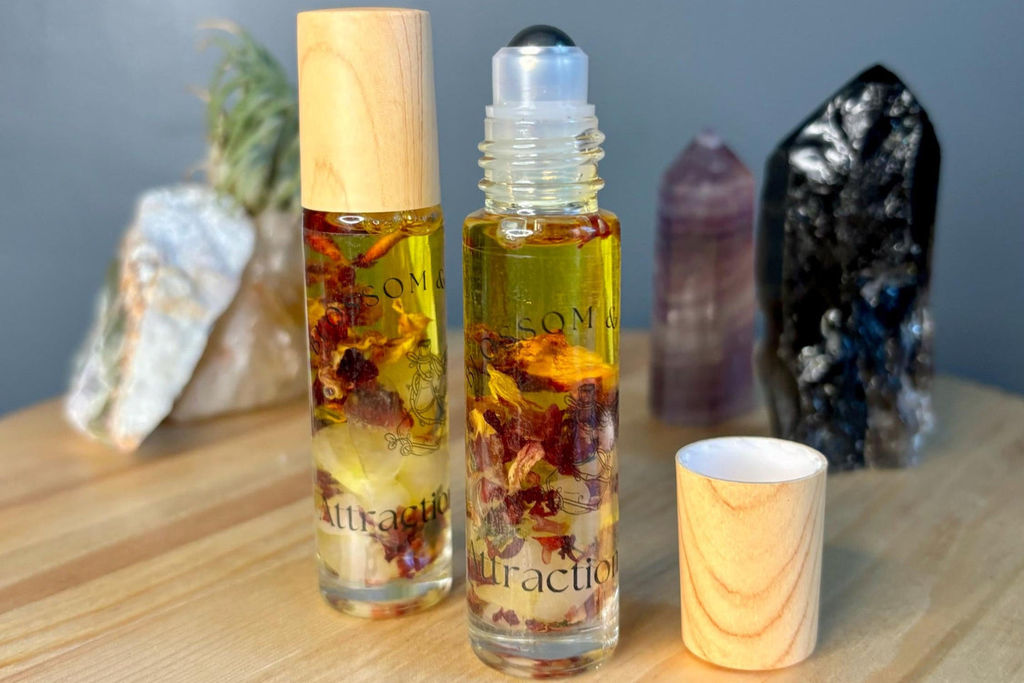 Two roller bottles of Attraction Oil. Bottles contain a golden yellow jojoba oil infused with rose petals and rose quartz.
