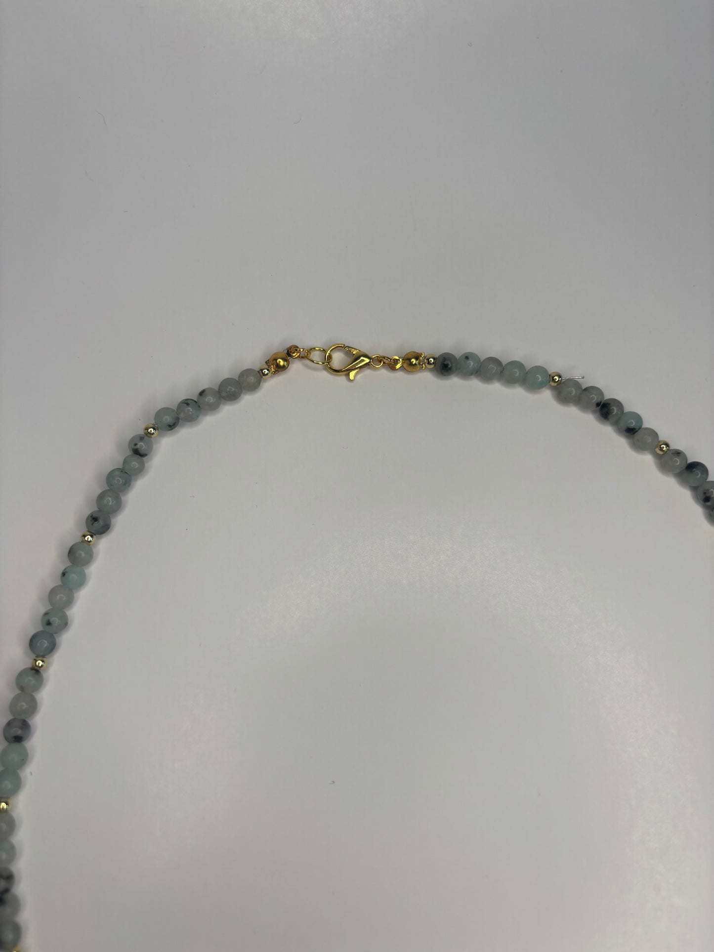 Necklace with speckled green beads and a gold clasp on a white background