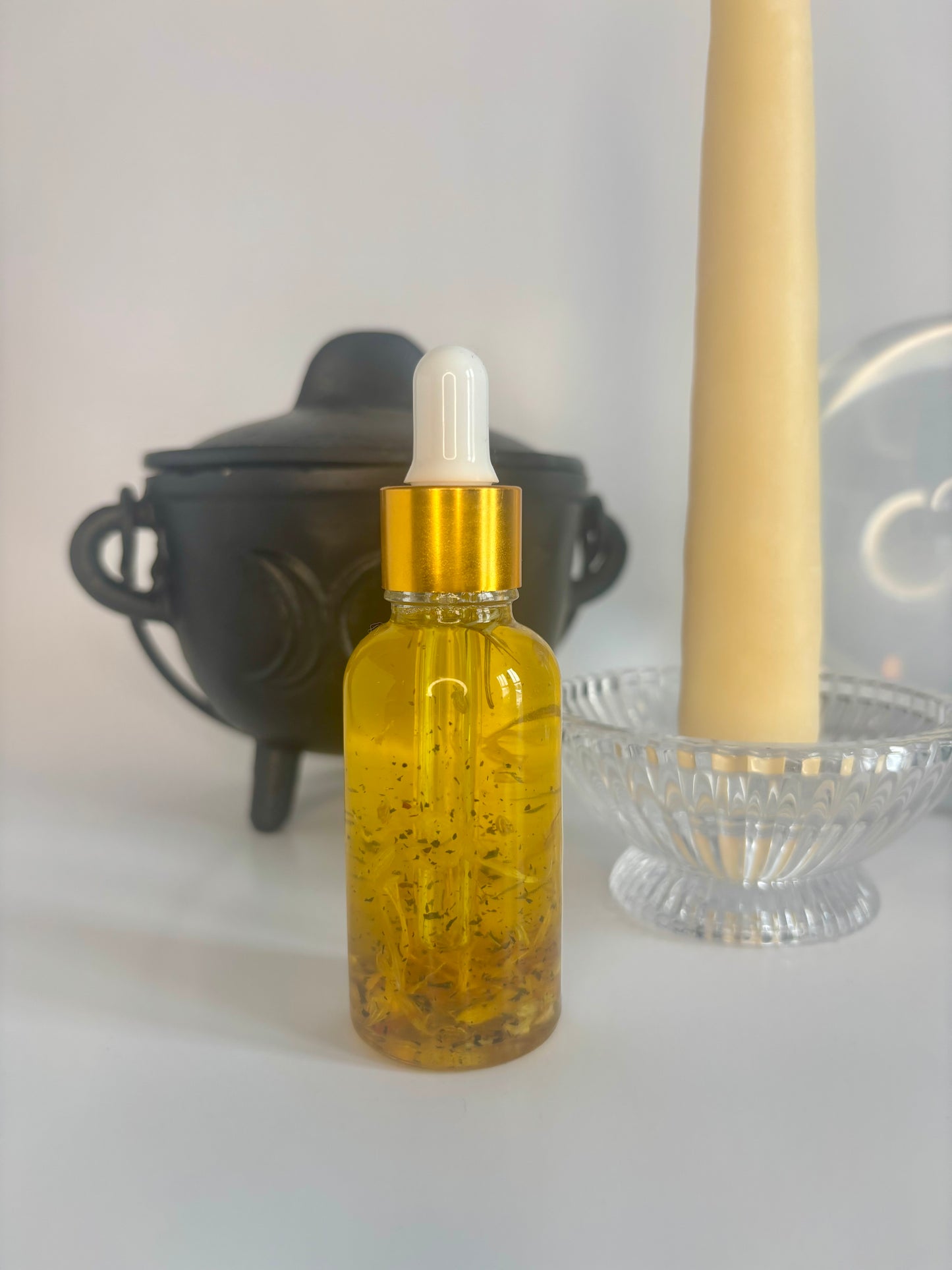 Clear dropper bottle with a gold cap, filled with golden oil and herbs on a white background.