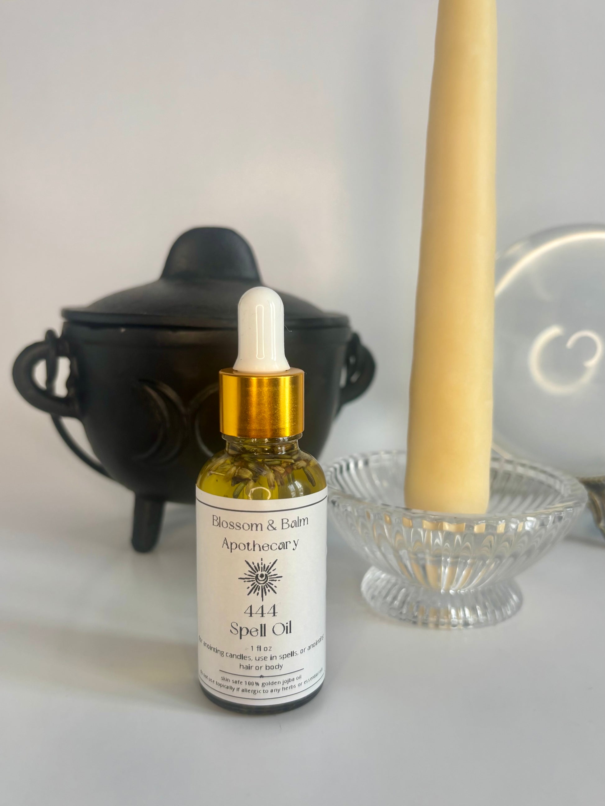 Bottle of 444 Spell Oil from Blossom & Balm Apothecary with a candle and black cauldron in the background.