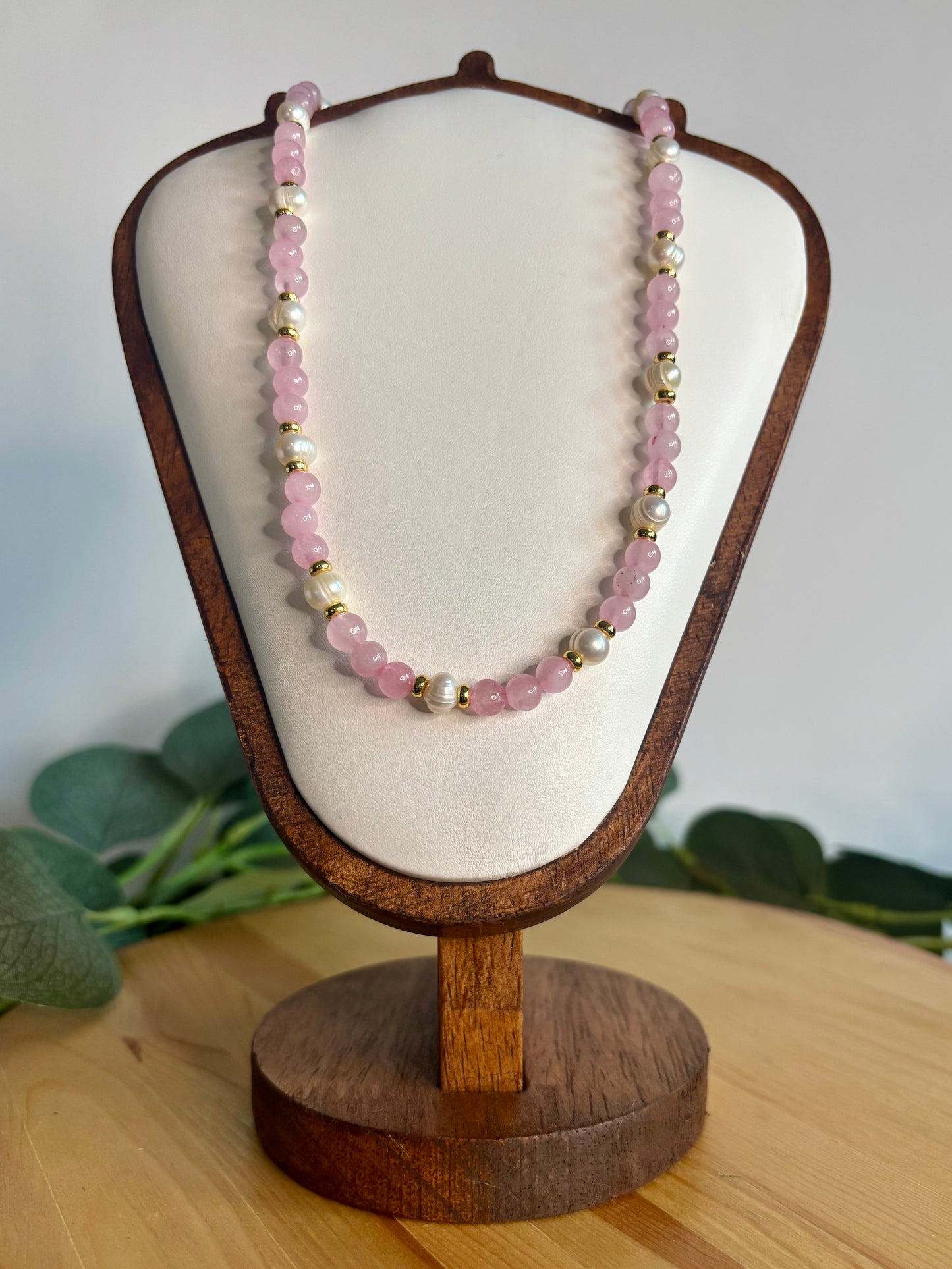 Necklace with rose quartz beads, freshwater pearls, and gold on a wooden stand against a light background