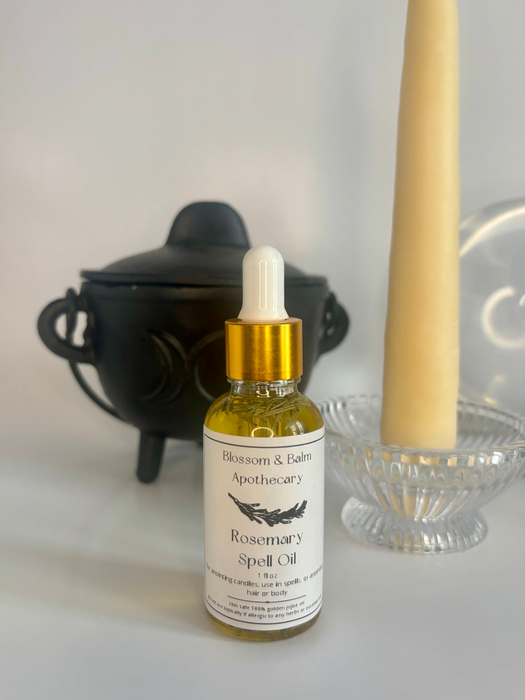 Bottle of Rosemary Spell Oil from Blossom & Balm Apothecary with a candle and black cauldron in the background.