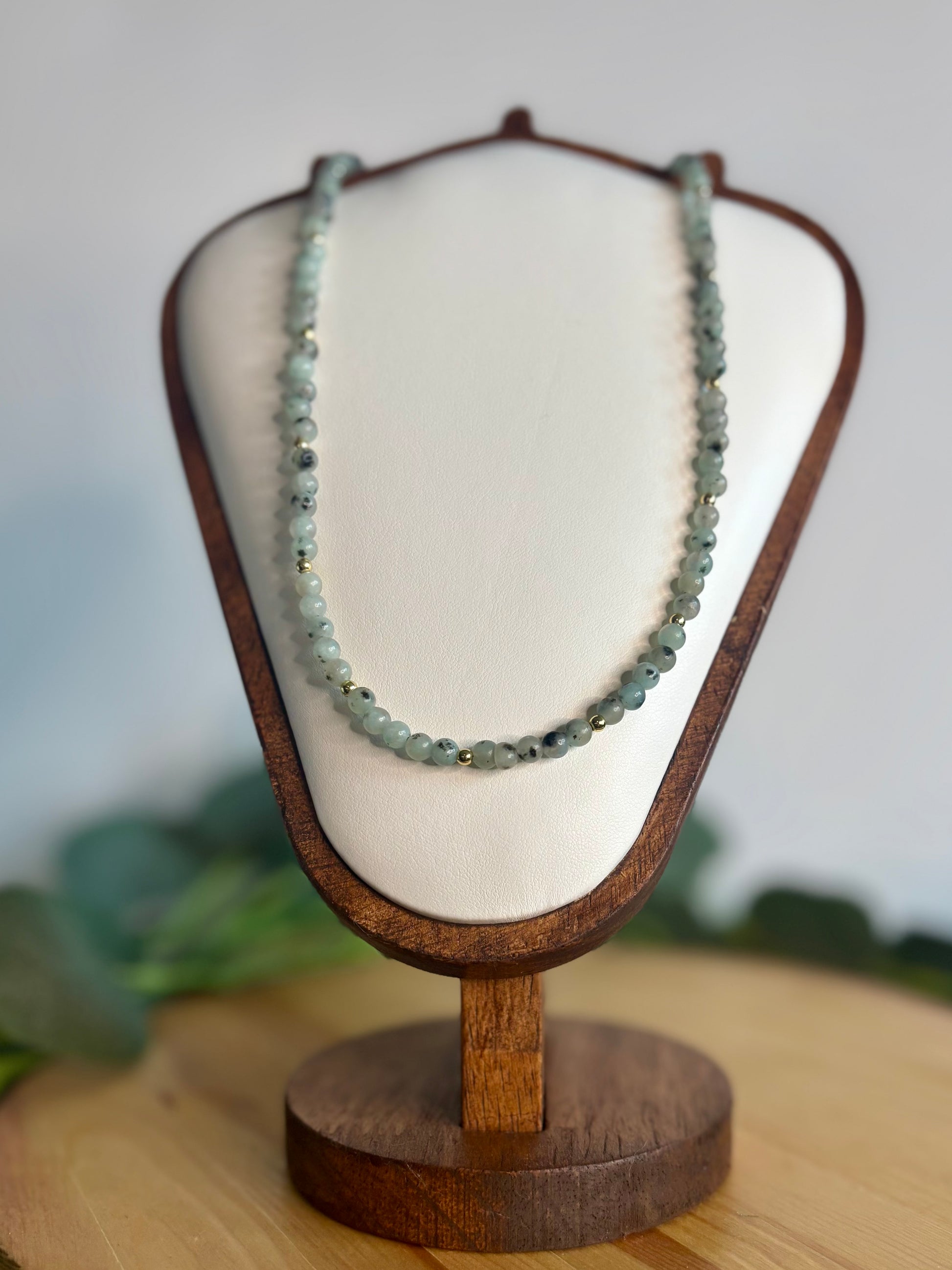 Sesame jasper beaded necklace on a wooden display stand with a blurred background