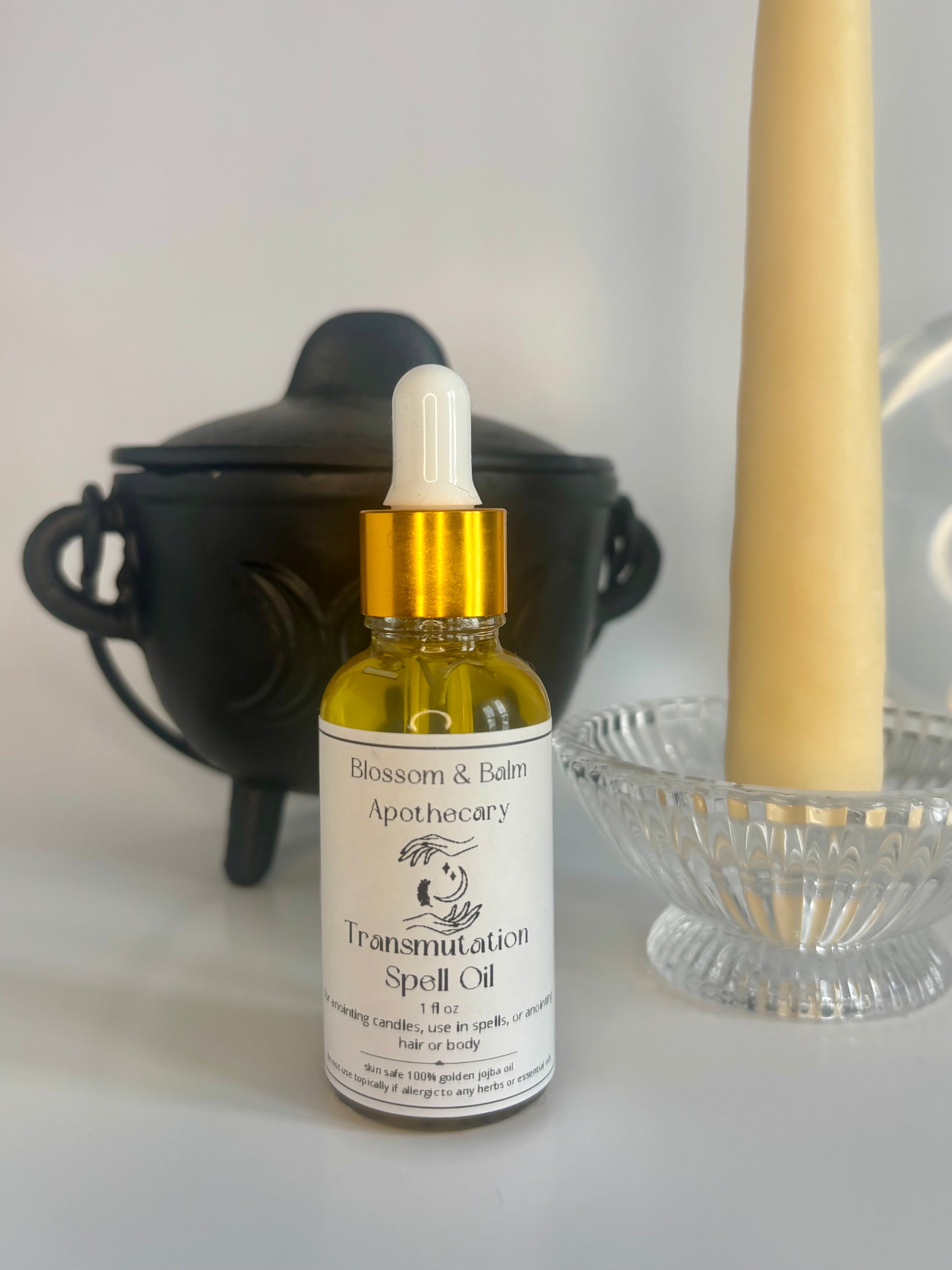 Bottle of 'Transmutation Spell Oil' from Blossom & Balm Apothecary with a dropper on a white surface.